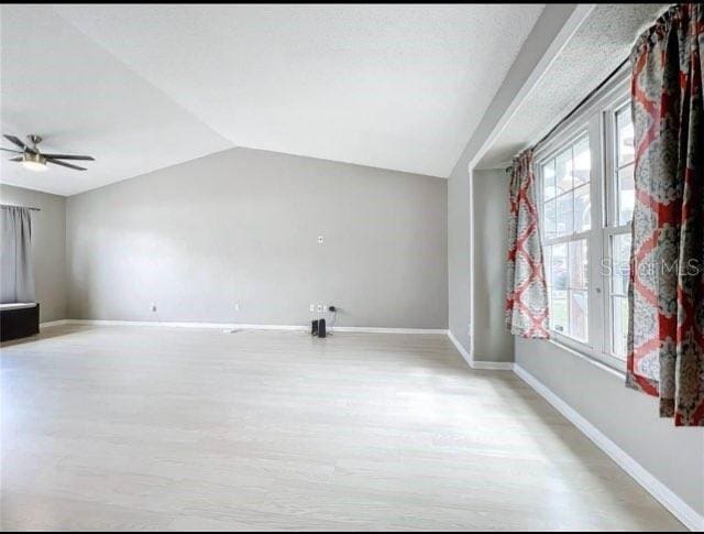 unfurnished living room featuring light wood-style floors, baseboards, ceiling fan, and vaulted ceiling