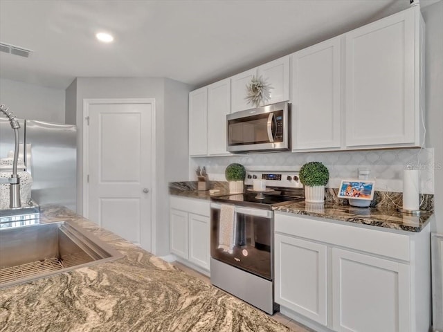 kitchen featuring dark stone counters, white cabinetry, visible vents, appliances with stainless steel finishes, and decorative backsplash
