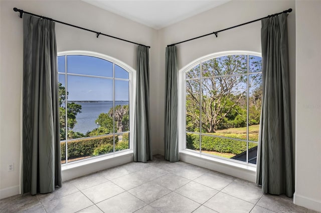 tiled empty room with a water view, baseboards, and a wealth of natural light
