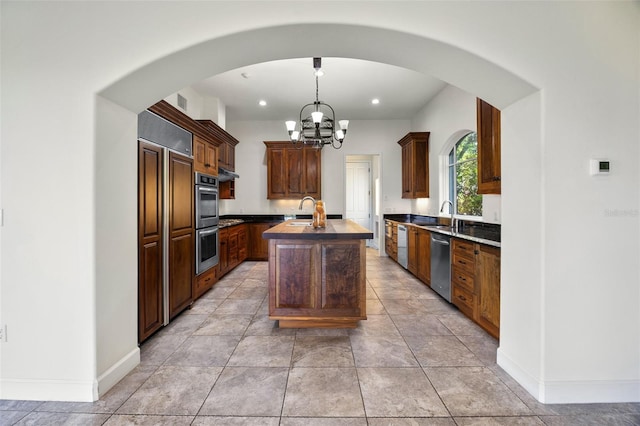 kitchen featuring a center island with sink, arched walkways, a sink, appliances with stainless steel finishes, and a notable chandelier