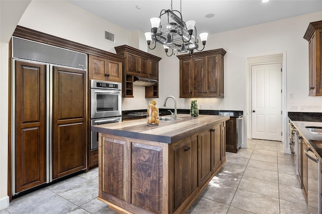 kitchen with an inviting chandelier, visible vents, butcher block countertops, an island with sink, and stainless steel appliances