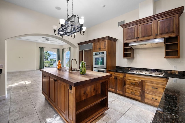 kitchen with open shelves, butcher block counters, under cabinet range hood, arched walkways, and appliances with stainless steel finishes