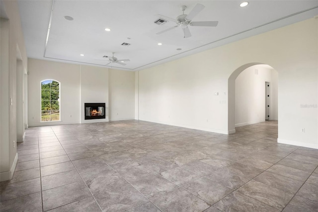 unfurnished living room featuring a ceiling fan, visible vents, arched walkways, a glass covered fireplace, and recessed lighting