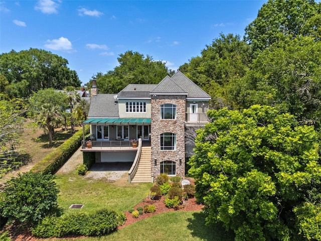 rear view of property featuring a standing seam roof, a chimney, a lawn, stairs, and stone siding