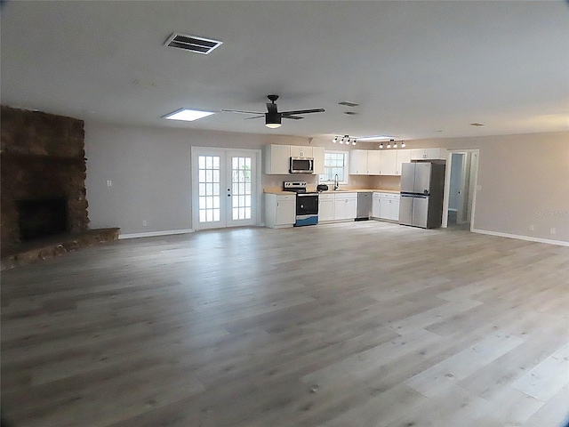 unfurnished living room featuring light wood-type flooring, visible vents, baseboards, and a sink