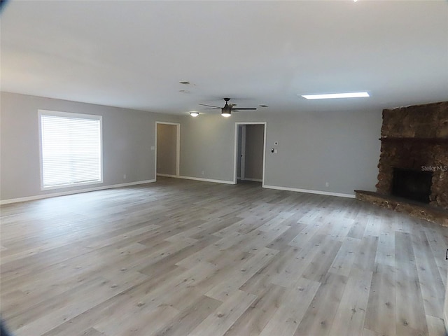 unfurnished living room featuring baseboards, a stone fireplace, a ceiling fan, and wood finished floors