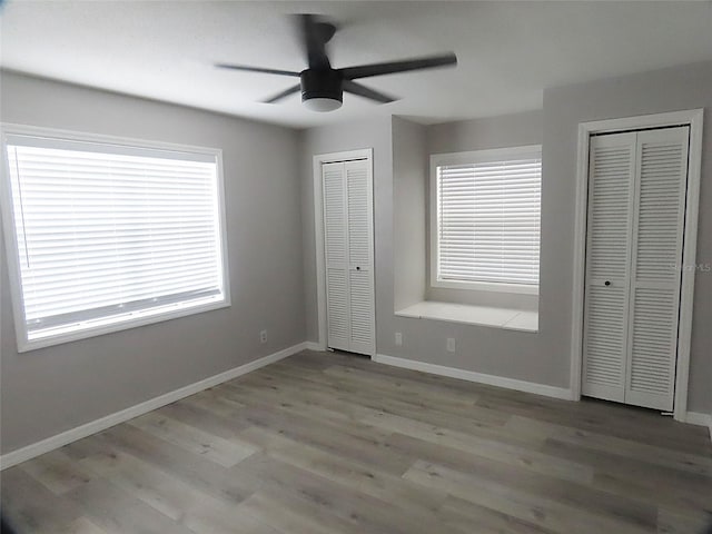 unfurnished bedroom featuring light wood-type flooring, ceiling fan, baseboards, and two closets