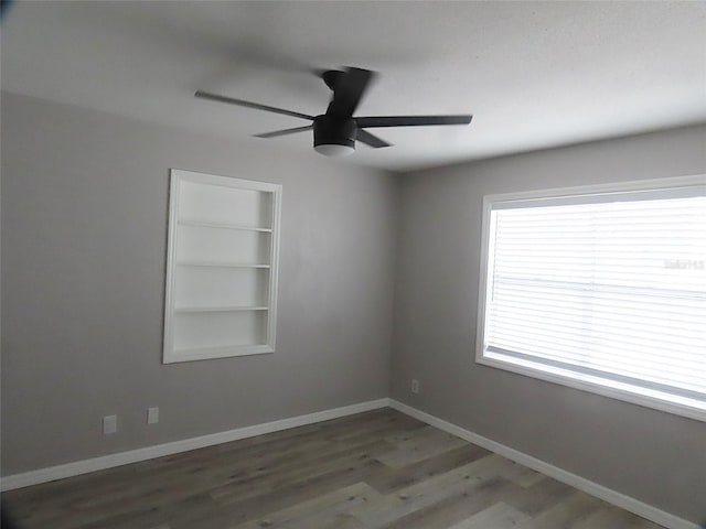 empty room with baseboards, ceiling fan, built in features, and wood finished floors