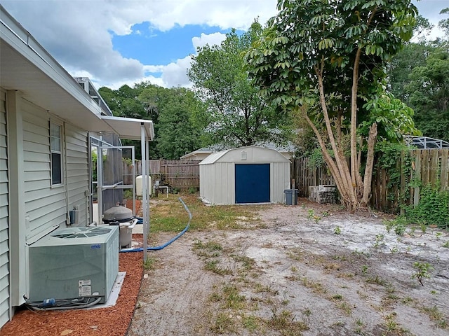 view of yard with a storage unit, a fenced backyard, cooling unit, and an outbuilding