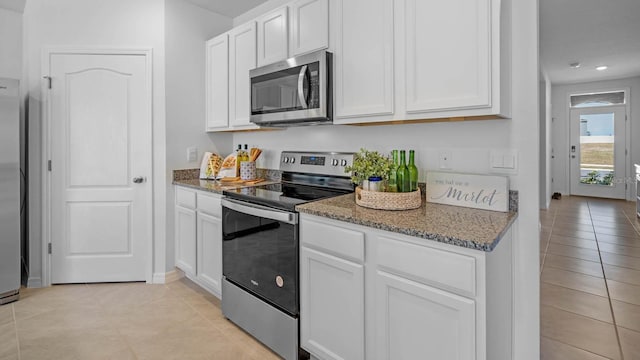 kitchen with stone countertops, white cabinetry, light tile patterned flooring, and stainless steel appliances