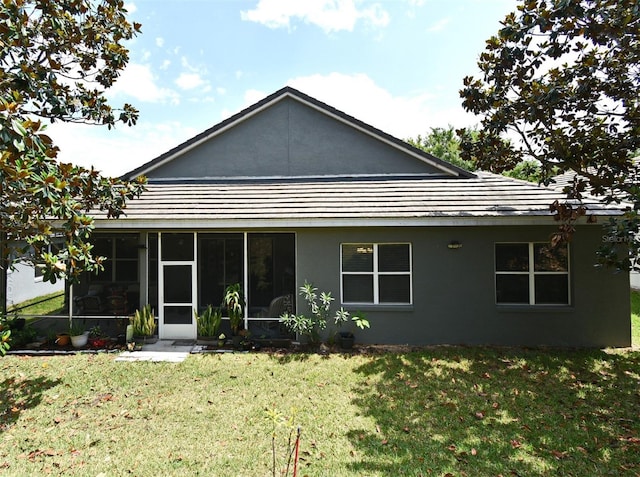 rear view of house featuring a yard, stucco siding, and a sunroom