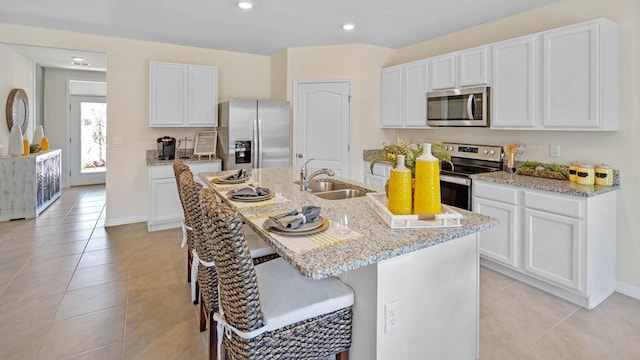 kitchen with white cabinets, stainless steel appliances, light stone counters, and a sink