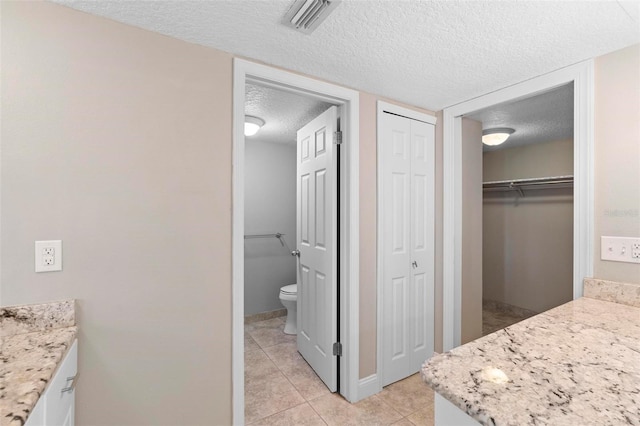 full bath featuring a closet, vanity, a textured ceiling, visible vents, and tile patterned floors