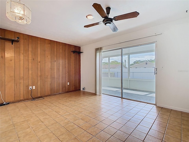 empty room featuring baseboards, wood walls, ceiling fan, and light tile patterned flooring