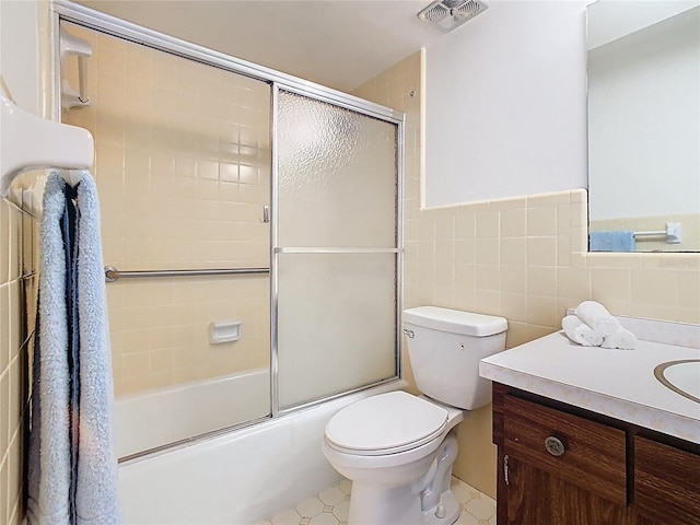 bathroom featuring toilet, tile walls, vanity, visible vents, and enclosed tub / shower combo