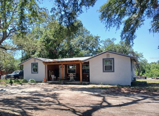 single story home featuring metal roof, a porch, and stucco siding