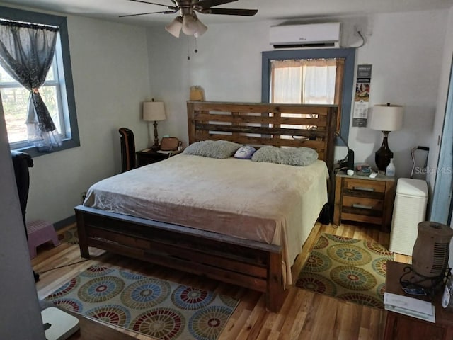 bedroom with a wall mounted air conditioner, wood finished floors, and a ceiling fan