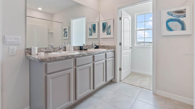 bathroom with double vanity, tile patterned floors, baseboards, and a sink