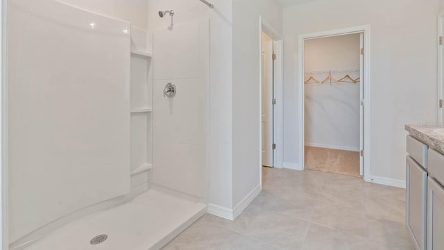 bathroom with a shower stall, a spacious closet, vanity, and baseboards