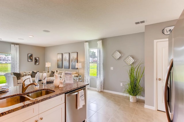 kitchen with stainless steel dishwasher, a sink, white cabinetry, open floor plan, and dark stone countertops