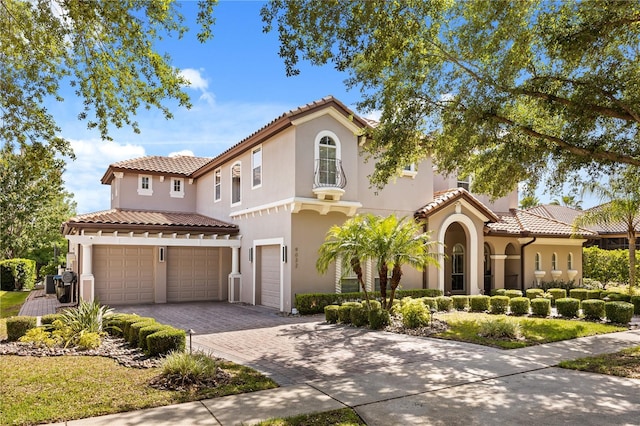 mediterranean / spanish-style house with an attached garage, a tiled roof, stucco siding, and decorative driveway