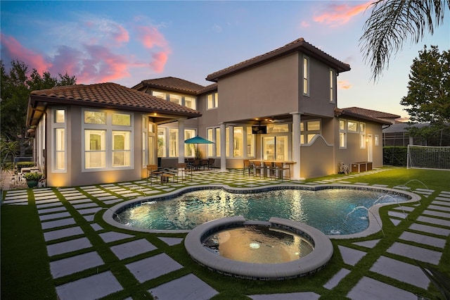 back of house featuring a tiled roof, fence, a pool with connected hot tub, a patio area, and stucco siding