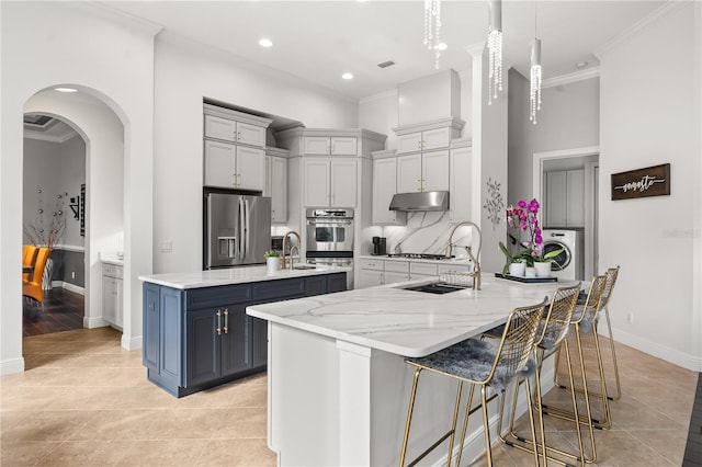 kitchen with crown molding, a large island with sink, under cabinet range hood, appliances with stainless steel finishes, and washer / clothes dryer