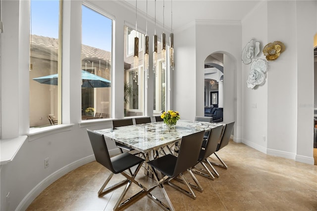 tiled dining room with ornamental molding, arched walkways, and baseboards