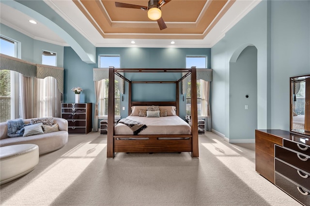 carpeted bedroom featuring a tray ceiling, crown molding, arched walkways, and baseboards