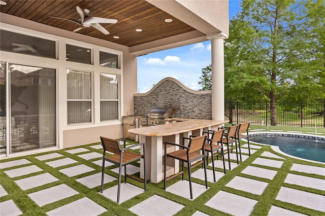 view of patio / terrace with fence, outdoor wet bar, grilling area, a ceiling fan, and an outdoor kitchen
