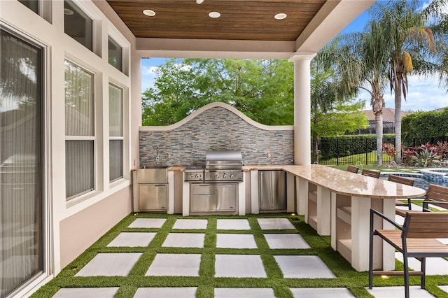 view of patio featuring area for grilling, exterior kitchen, fence, and outdoor wet bar