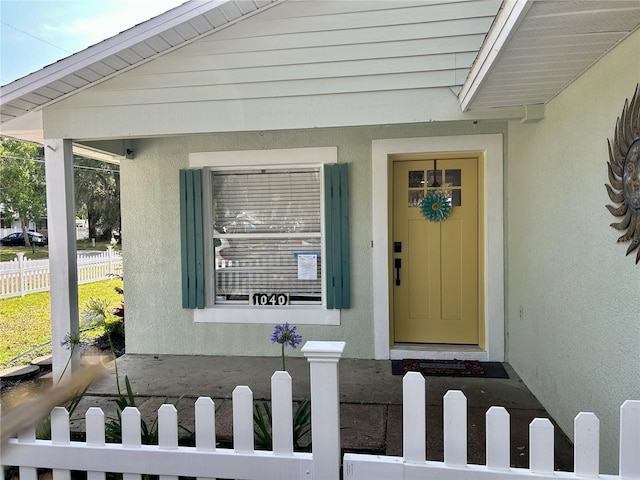 view of exterior entry with stucco siding and fence