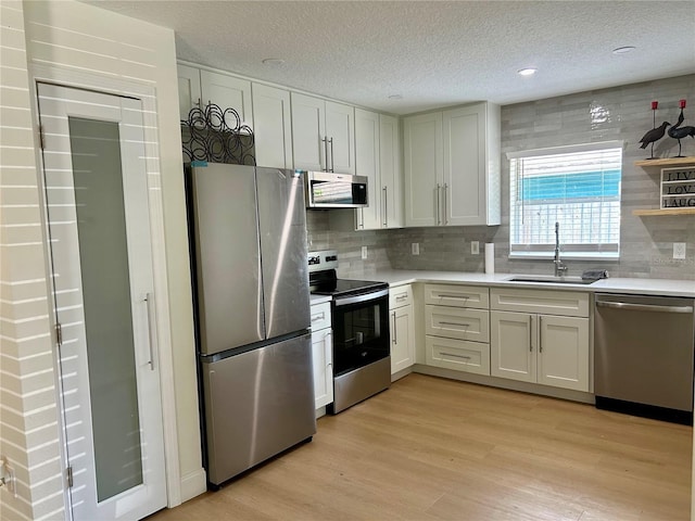 kitchen featuring appliances with stainless steel finishes, a sink, light countertops, a textured ceiling, and tasteful backsplash