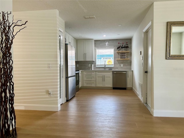 kitchen featuring appliances with stainless steel finishes, baseboards, light wood finished floors, light countertops, and a textured ceiling