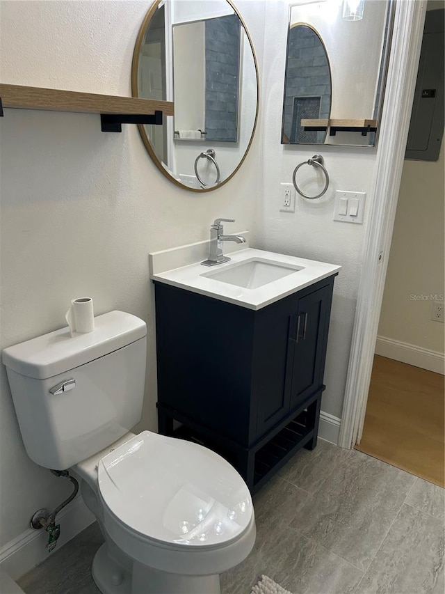 bathroom with electric panel, toilet, vanity, and baseboards