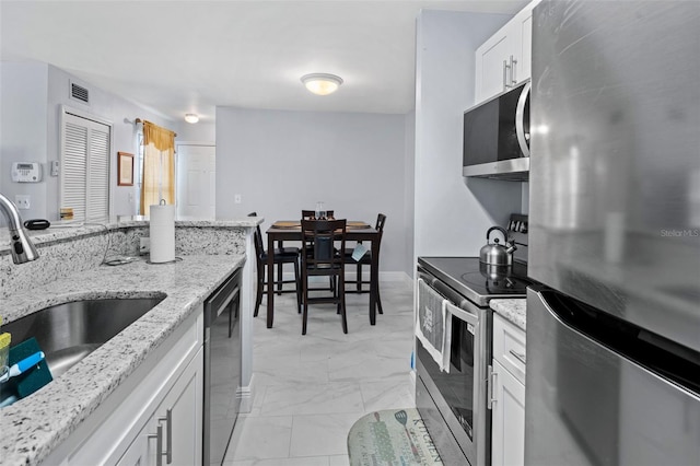 kitchen with a sink, stainless steel appliances, white cabinetry, visible vents, and marble finish floor