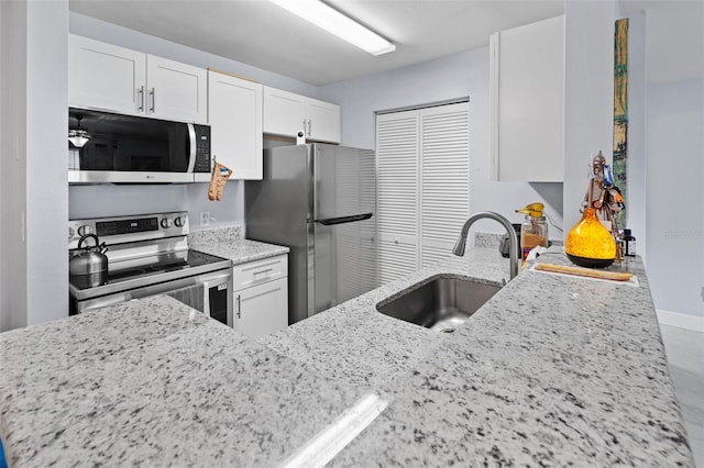 kitchen with a sink, white cabinets, baseboards, light stone countertops, and appliances with stainless steel finishes
