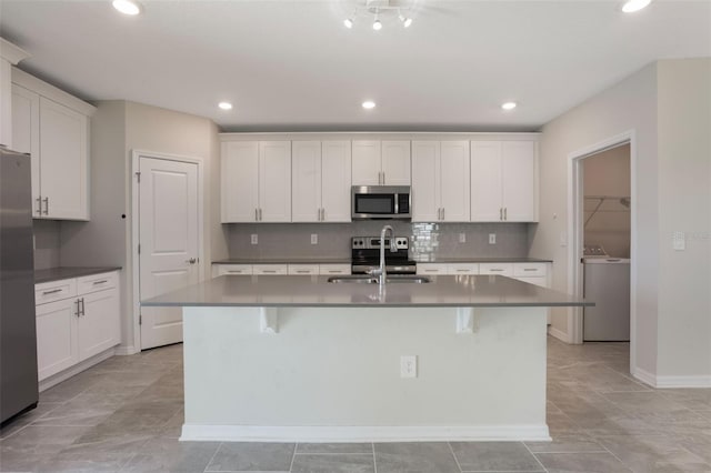 kitchen with a sink, a kitchen island with sink, backsplash, washer / dryer, and appliances with stainless steel finishes