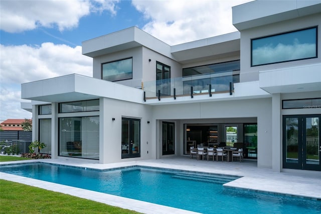 back of house with a balcony, an outdoor pool, stucco siding, and french doors