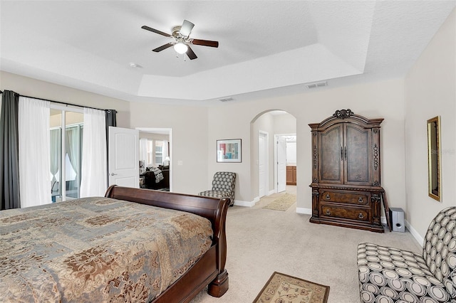 bedroom featuring light colored carpet, visible vents, arched walkways, a tray ceiling, and baseboards