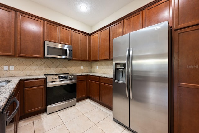 11908 Fiore Dr Unit 1, Orlando, FL 32827 - kitchen with stainless steel appliances, light tile patterned floors, backsplash, light stone counters, and a textured ceiling
