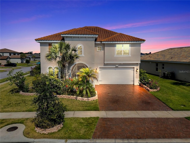mediterranean / spanish-style house with a garage, stucco siding, a tiled roof, decorative driveway, and a front lawn