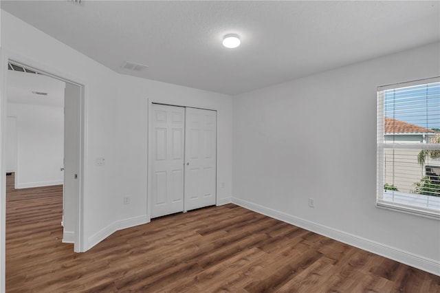 unfurnished bedroom with wood finished floors, baseboards, and a closet