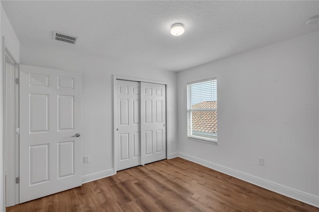 unfurnished bedroom with wood finished floors, baseboards, a closet, and a textured ceiling