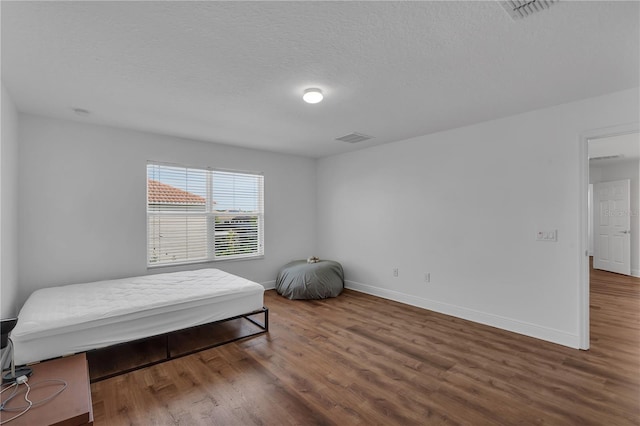 bedroom with wood finished floors, baseboards, and a textured ceiling