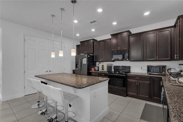 kitchen featuring black appliances, light tile patterned floors, a breakfast bar, a kitchen island, and dark brown cabinetry