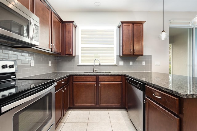 kitchen with stainless steel appliances, a sink, a peninsula, light tile patterned flooring, and dark stone counters
