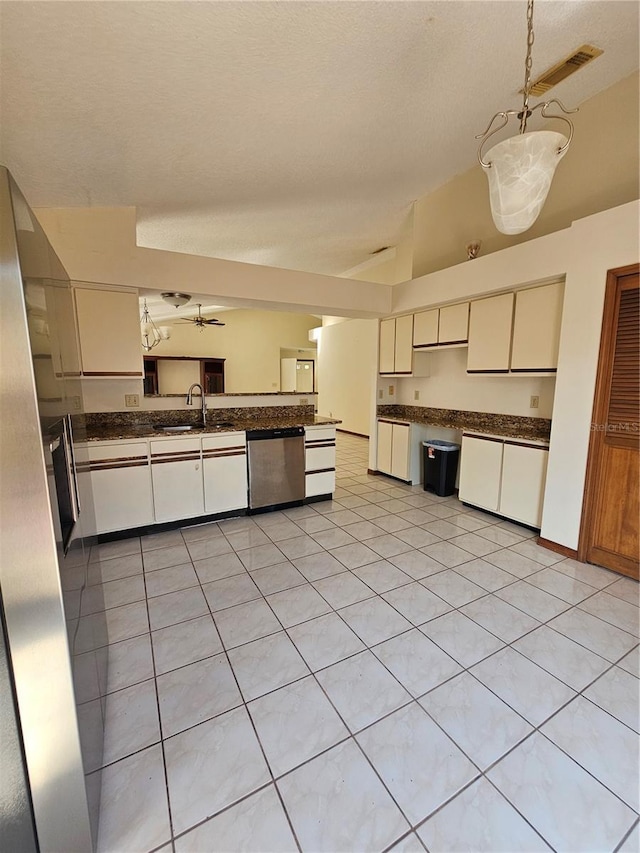 kitchen with stainless steel appliances, dark countertops, a sink, light tile patterned floors, and cream cabinetry