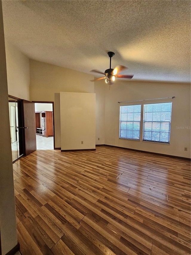 unfurnished living room with lofted ceiling, a ceiling fan, a textured ceiling, wood finished floors, and baseboards