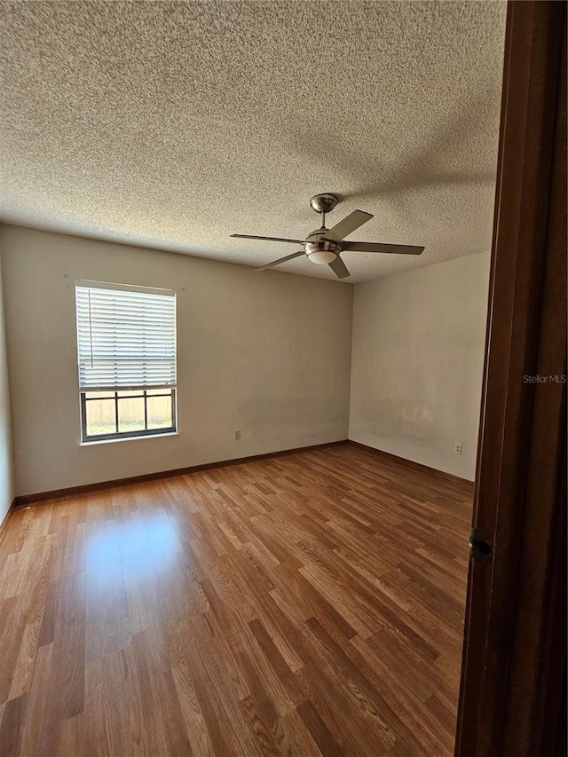 spare room with wood finished floors, a textured ceiling, ceiling fan, and baseboards